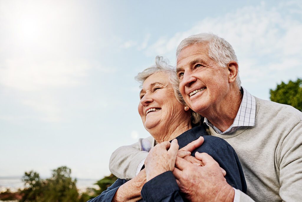 Elderly couple hugging and smiling outside.