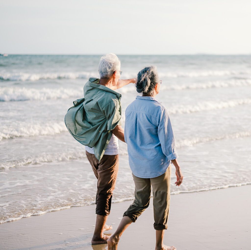 Elderly couple walking on the beach at sunset.