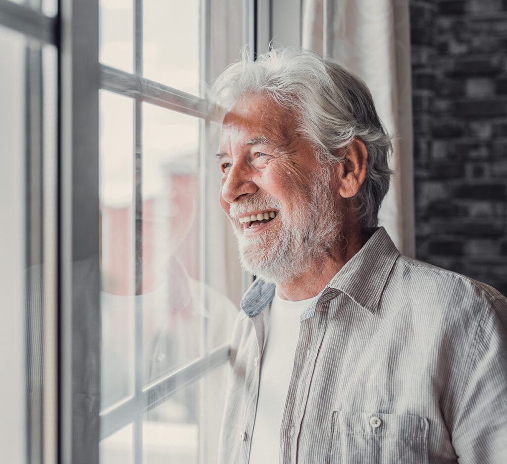 Happy older man looking out of window away with hope.
