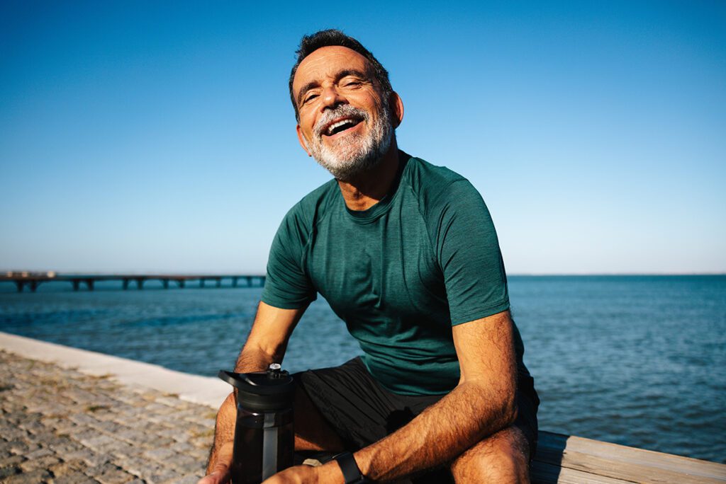 Smiling man enjoying outdoors by a scenic waterfront.