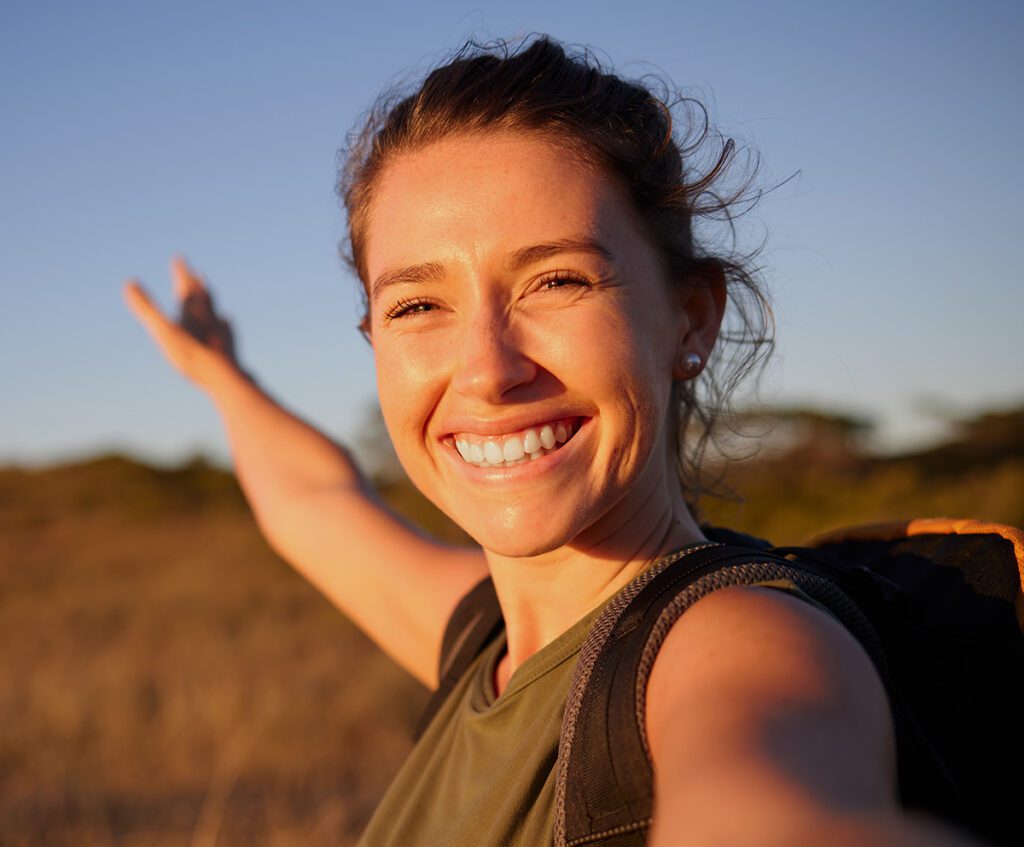 Women smiling outside with the sun shining on her.