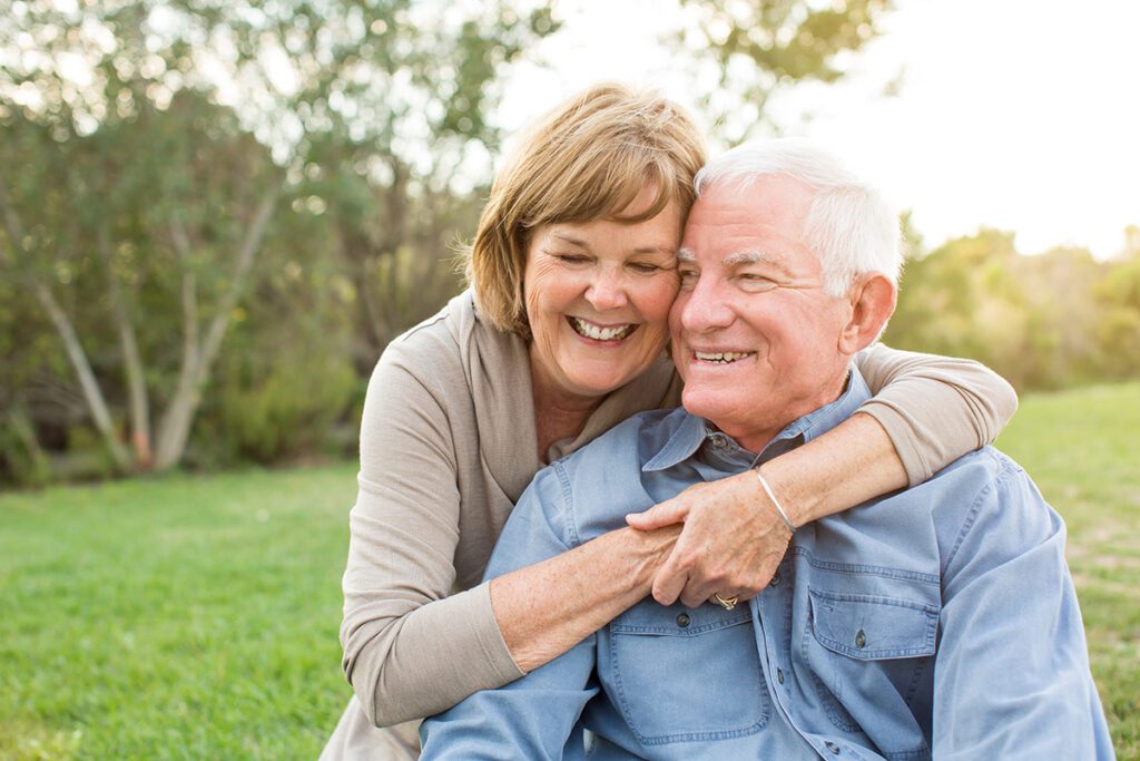 older couple hugging smiling outside at-a park