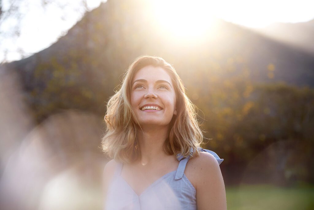 Women smiling looking up at the sky with the sun shining in background.