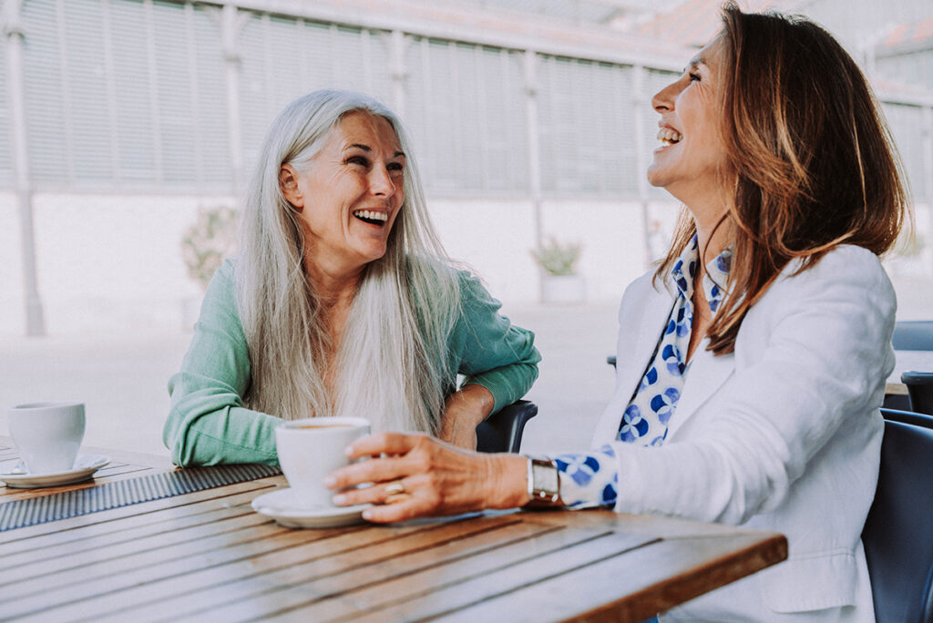 two women outdoors having coffee smiling and laughing